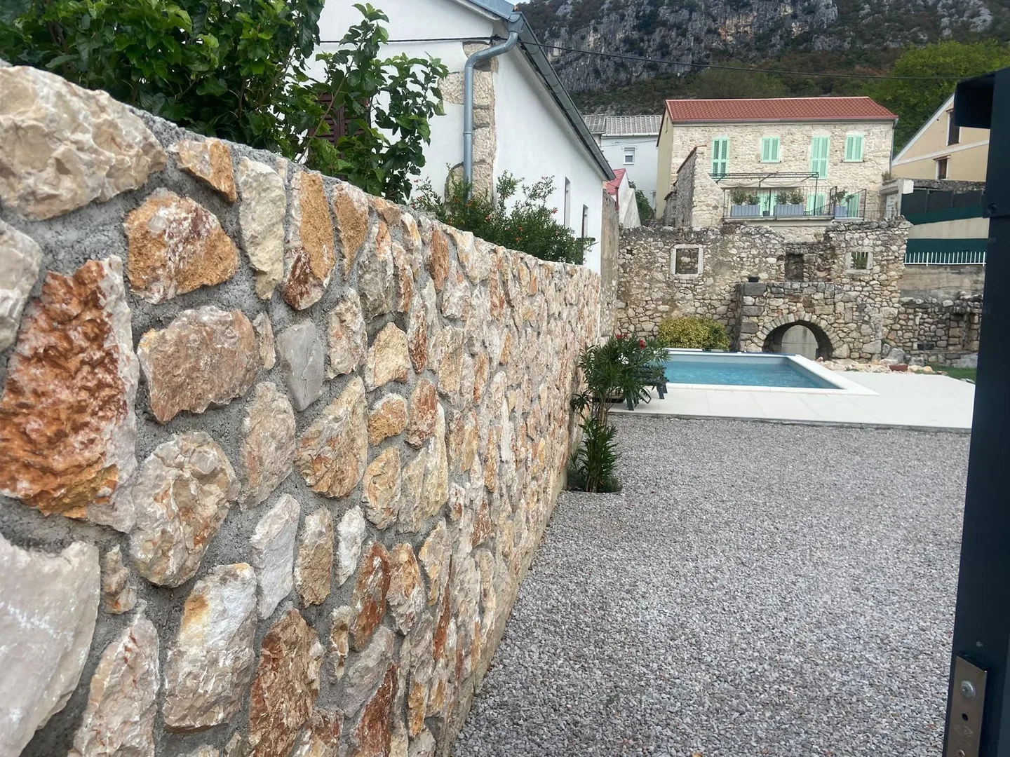 A stone wall along the gravel drive towards the pool