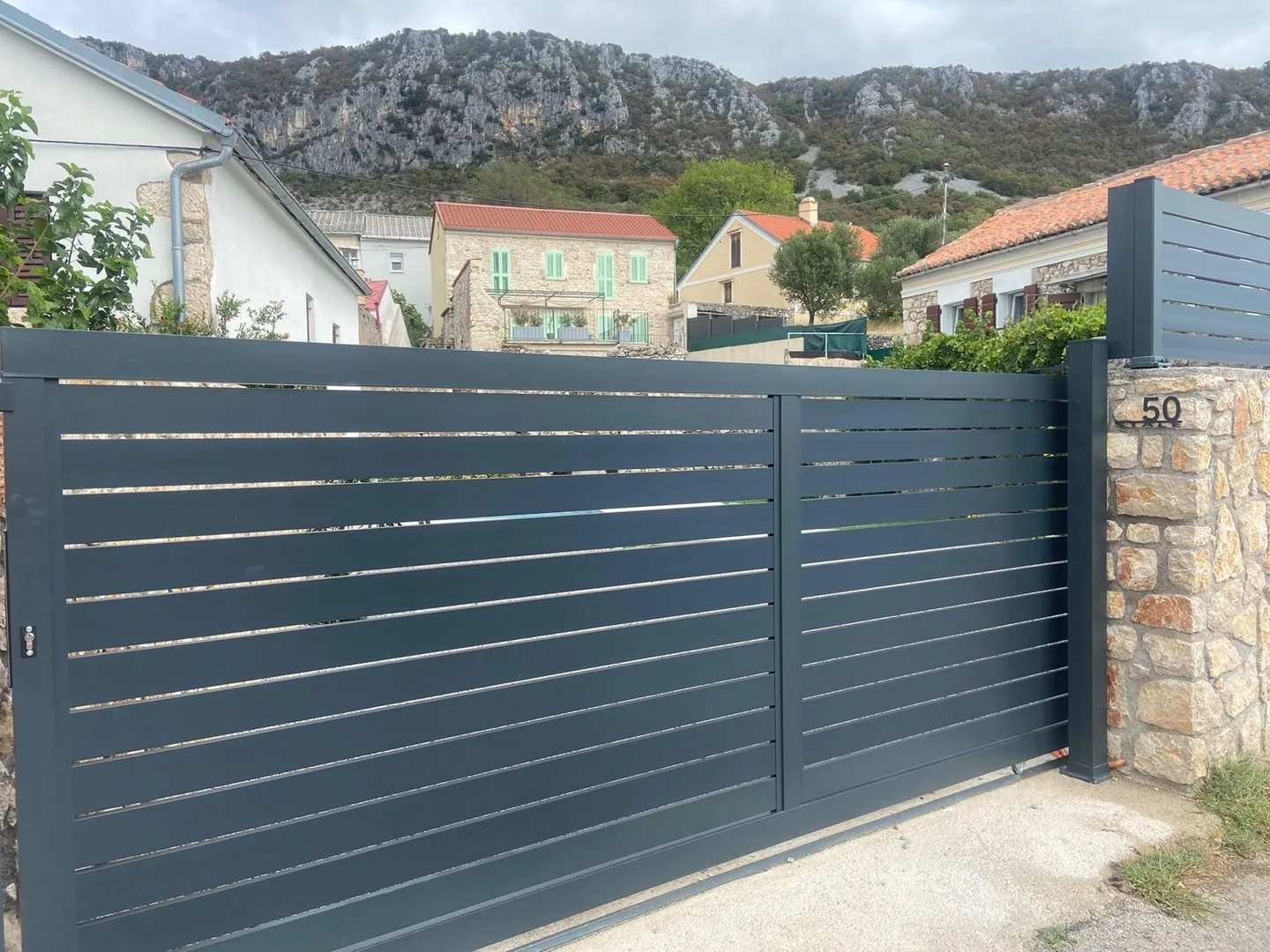 The grey sliding gate at number 50, the village and the mountain above it