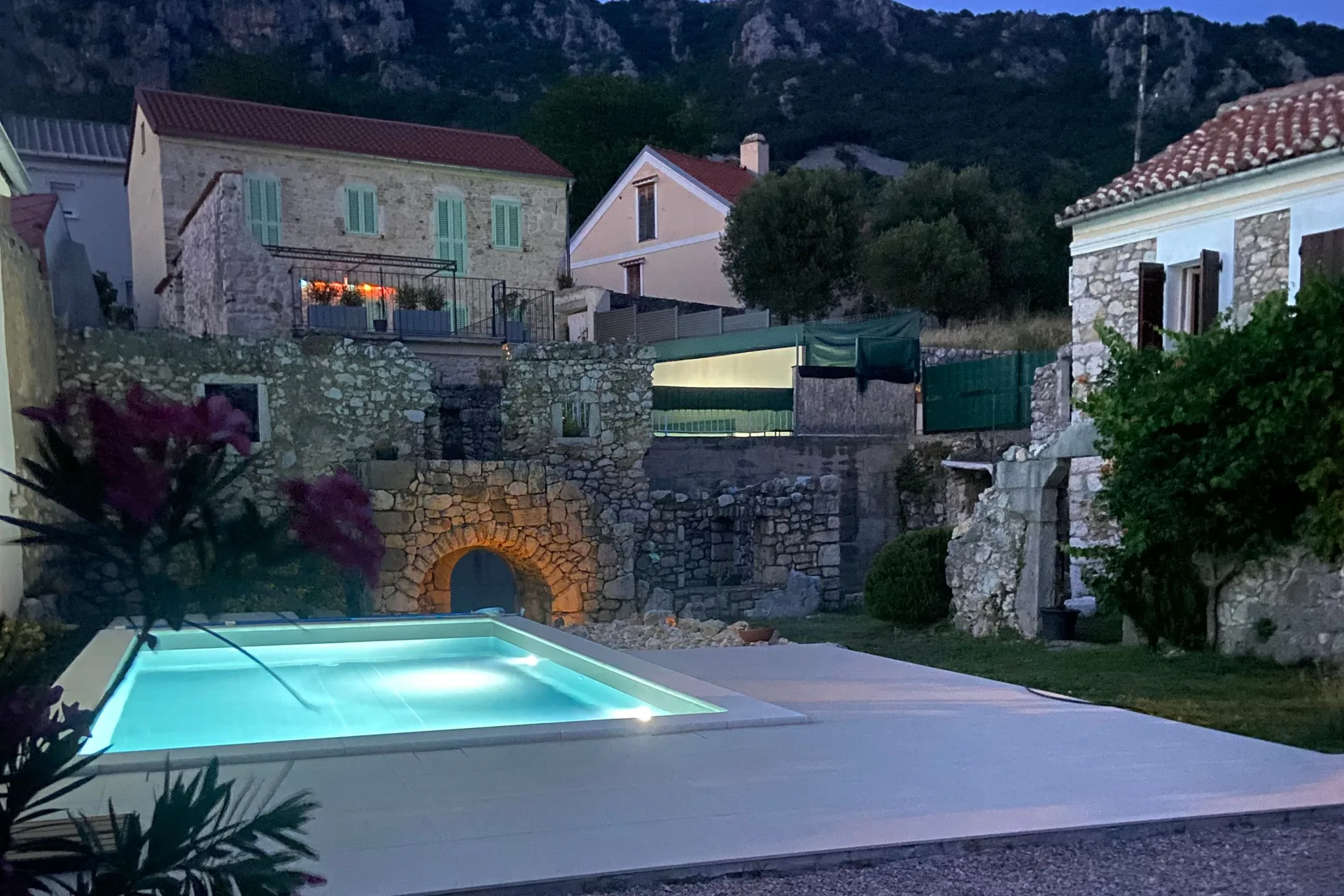 The lit pool at dusk, the ruin’s arch glowing behind it and the balcony lights of the house above