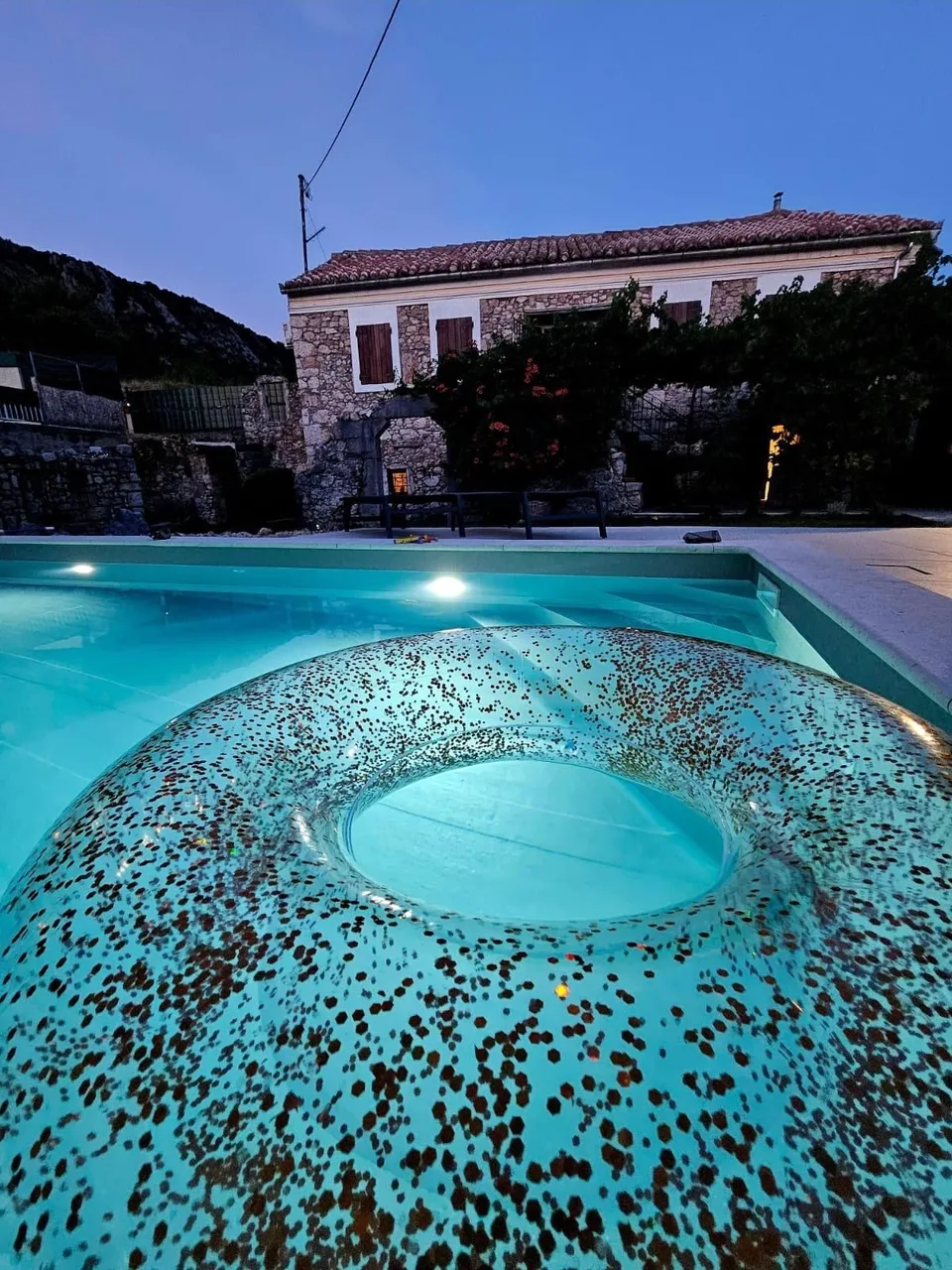 The pool lit at night, seen from above, the house behind