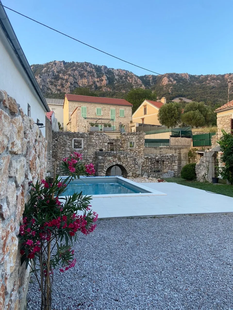 The pool behind a stone wall and oleander, the ruin and the village beyond