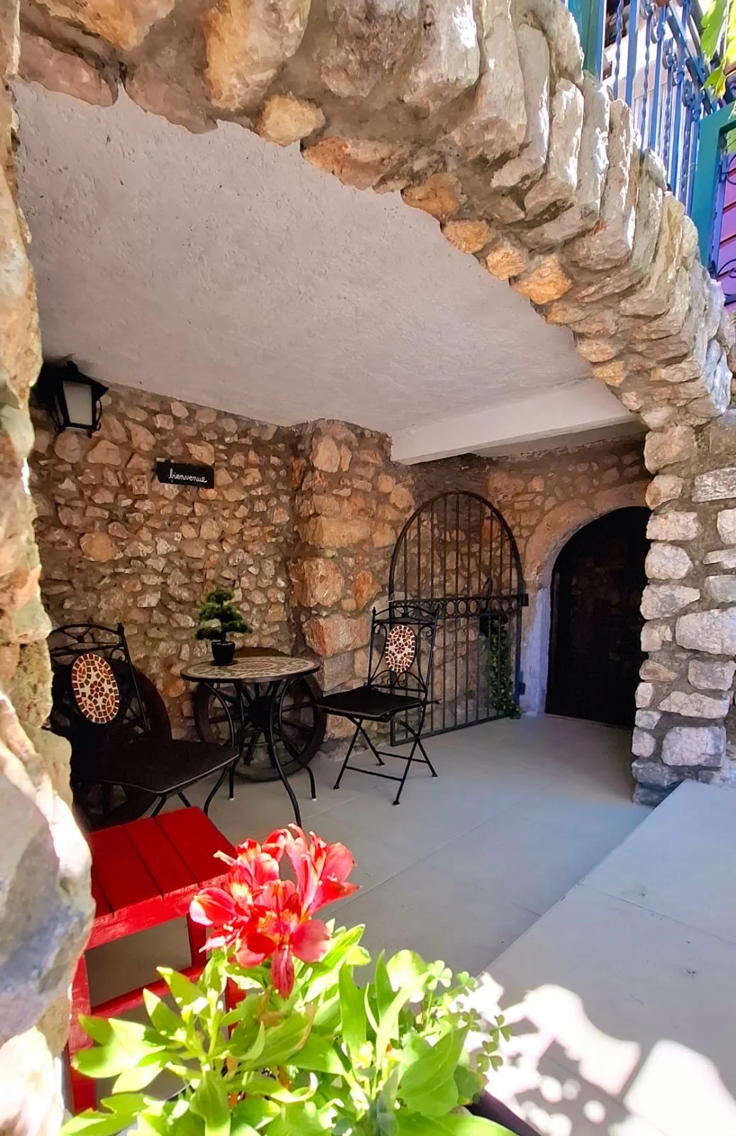 The alcove under the stairs: a mosaic bistro table, two chairs and an arched wrought-iron gate
